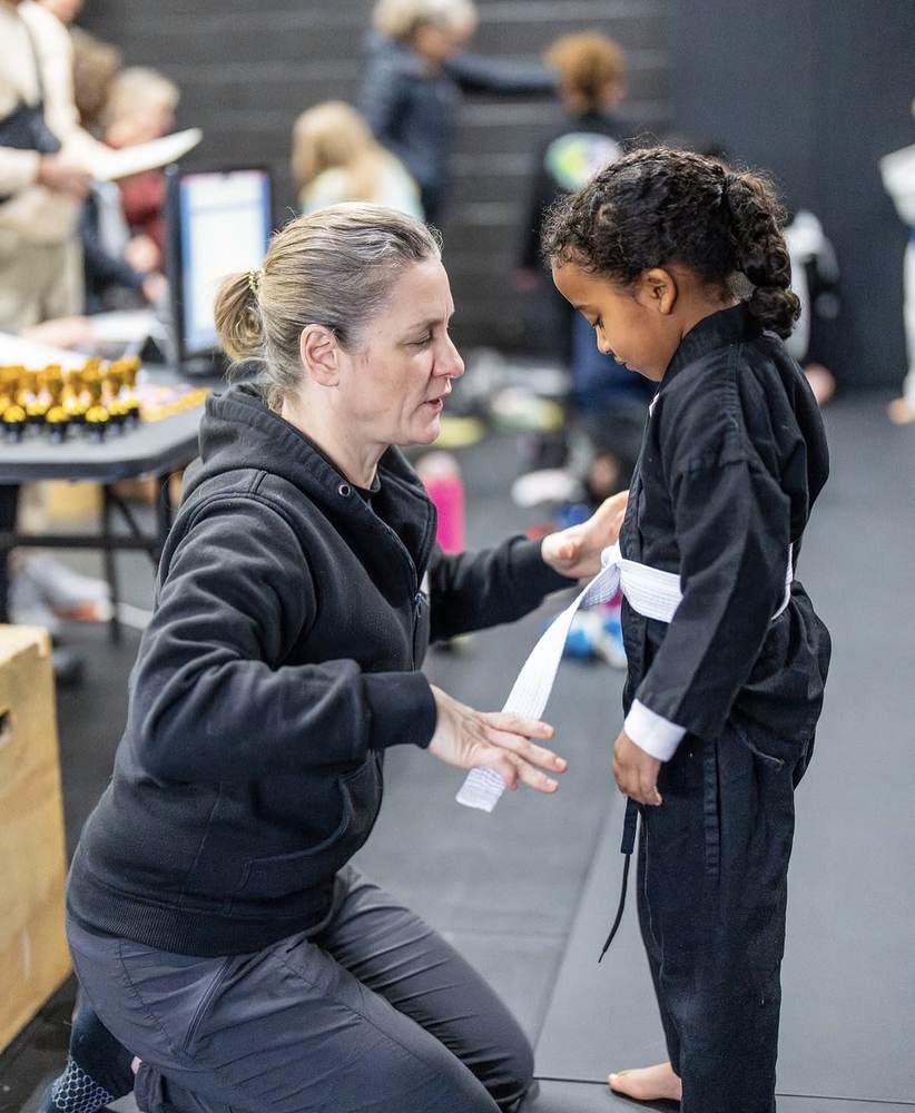 A coach tying a young student's belt at WDC BJJ Hyattsville